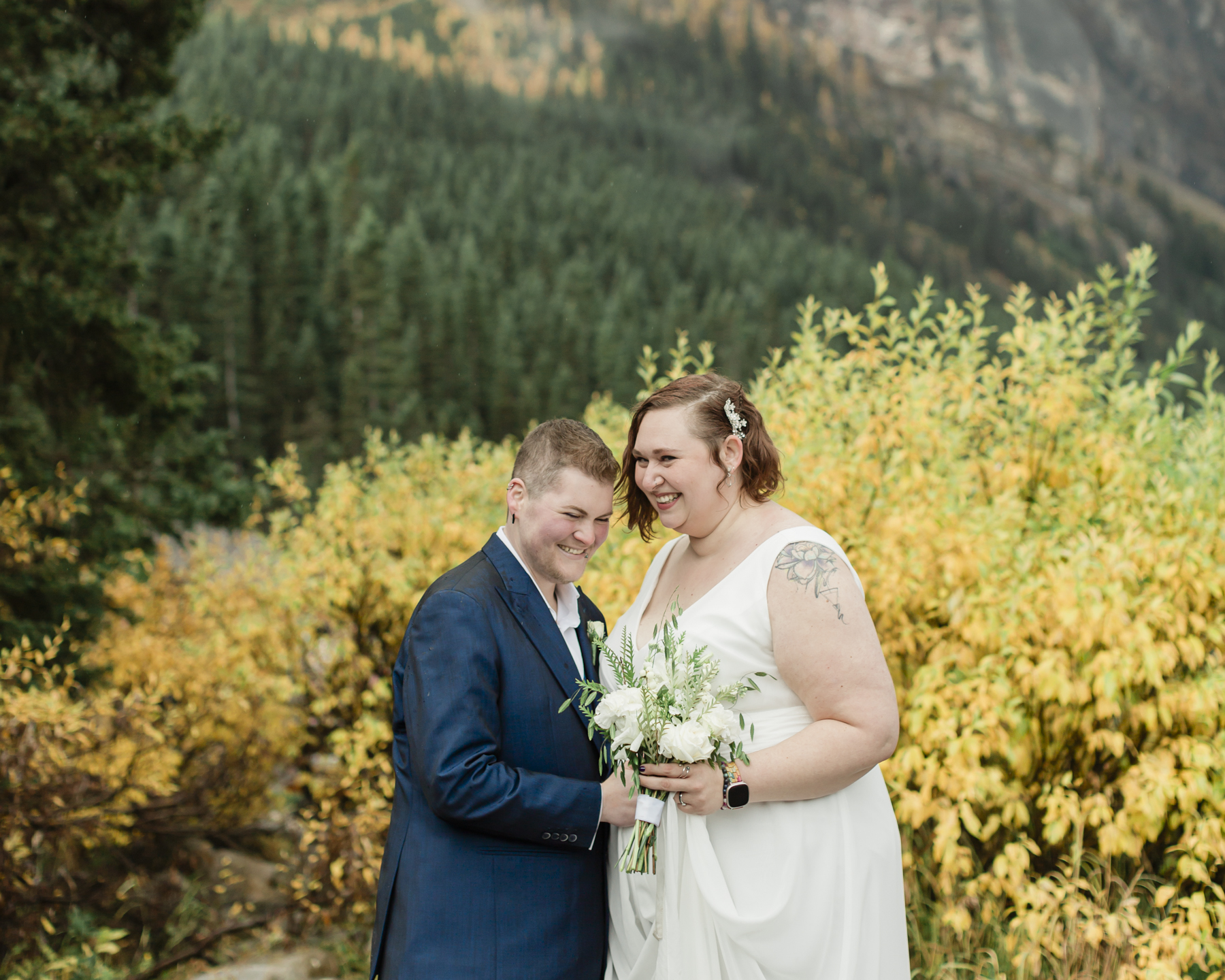 A LGBTQIA+ couple laughing together at Lake Louise in autumn