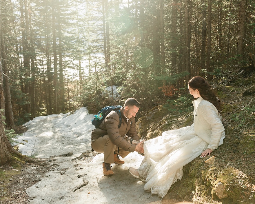 an eloping couple stops during their hike to tie shoes