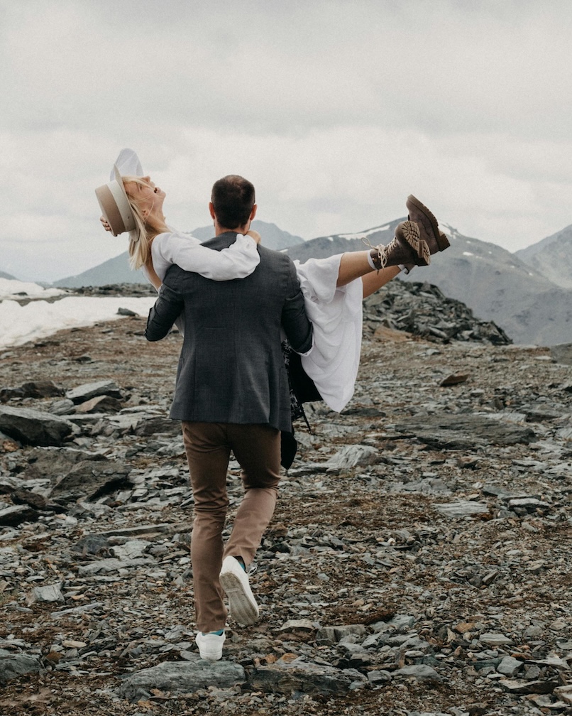 groom carries bride through mountains during winter elopement photoshoot