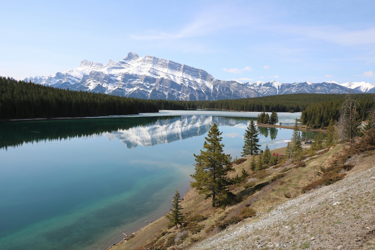 A snowy mount rundle sits behind a perfectly clear and still lake