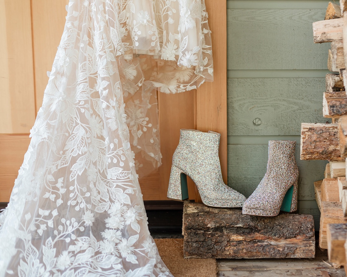 sparkly heeled booties rest on a log next to the train of a wedding dress for a moraine lake elopement