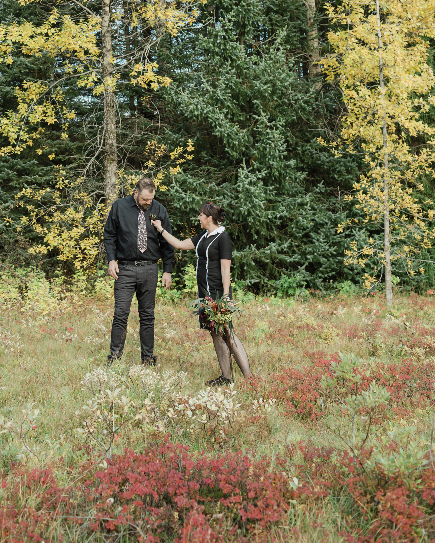 Wedding couple's portraits in the Iceland forest, the bride is holding her bouquet and fixing his tie