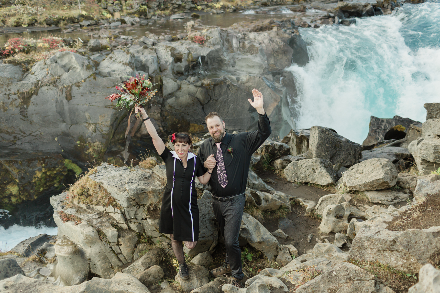 Virginia and Derek's arms in the air and celebrating their elopement ceremony in front of a running waterfall in Iceland on the Golden Circle