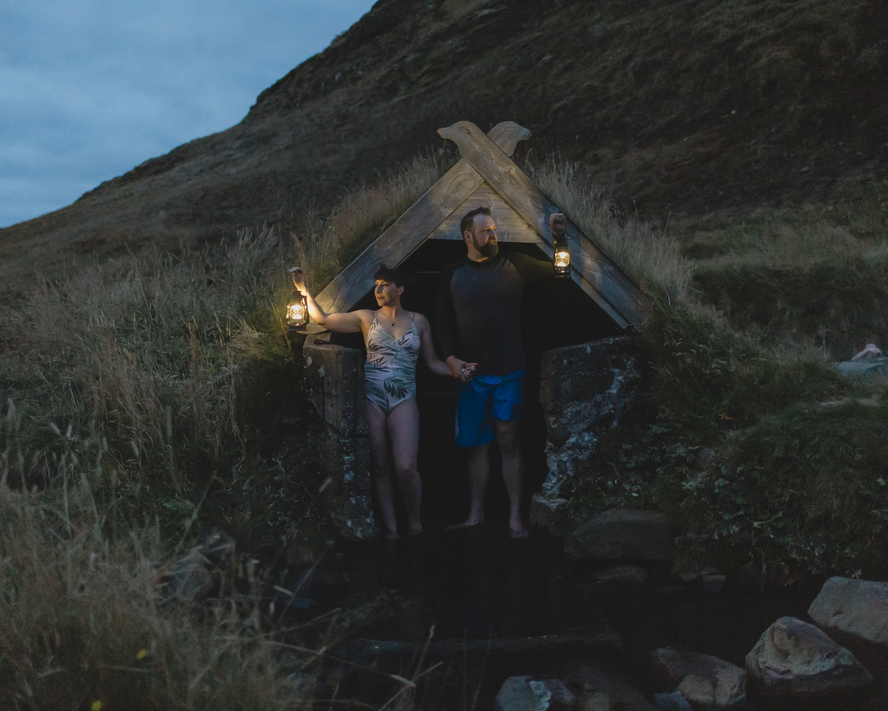 The couple is holding lanterns while standing by an Iceland hot spring after their elopement 