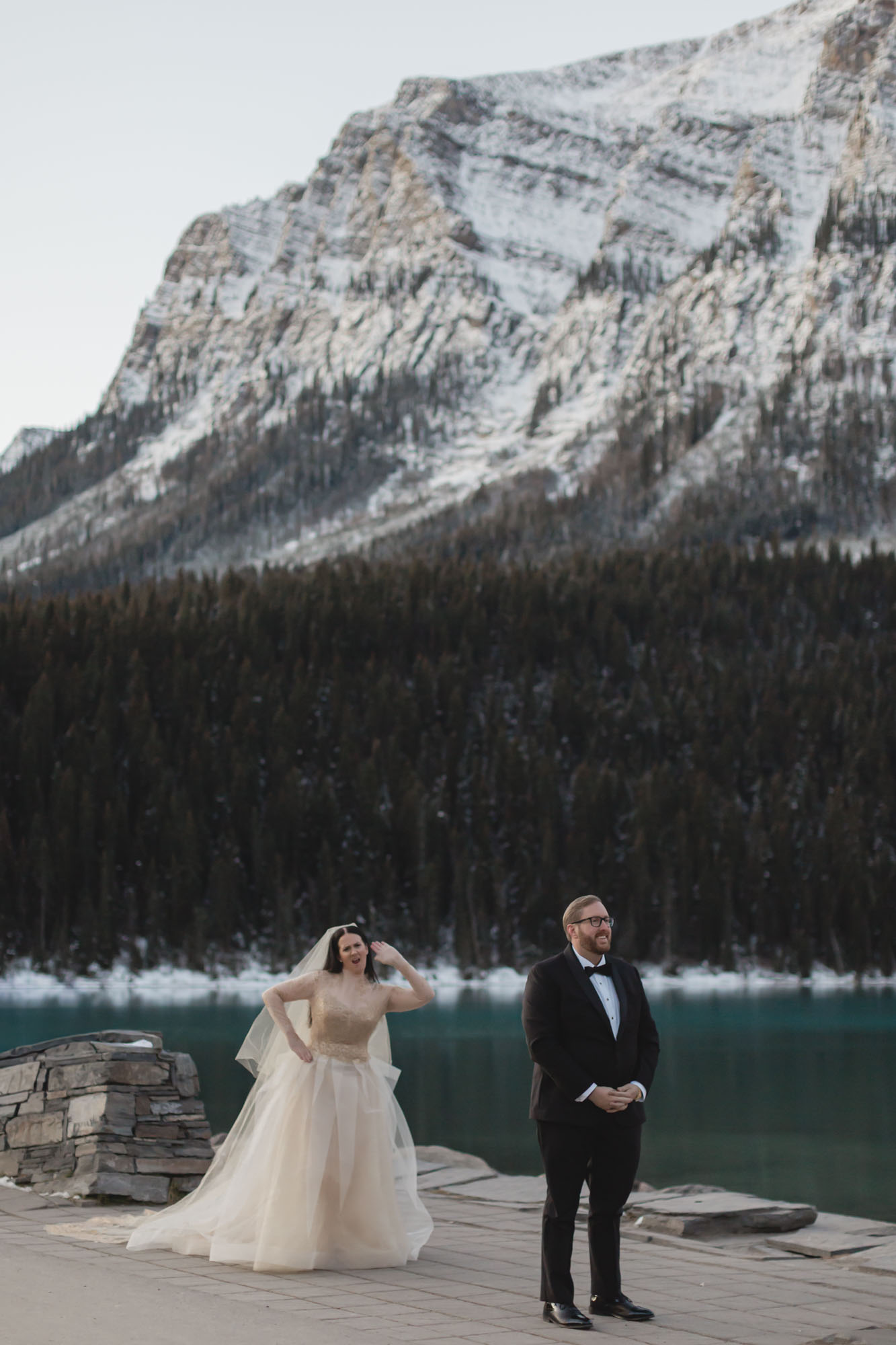 Lake Louise elopement in Banff National Park, the couple is about to have their first look, the bride is dancing goofy behind the groom and he's smiling, waiting for her to approach him