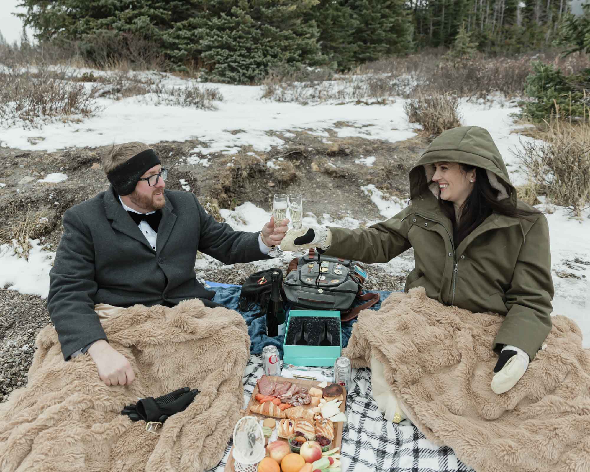 Wedding couple enjoying a winter picnic at Bow Lake in Banff National Park during their Elopement, featuring diet coke and a charcuterie board