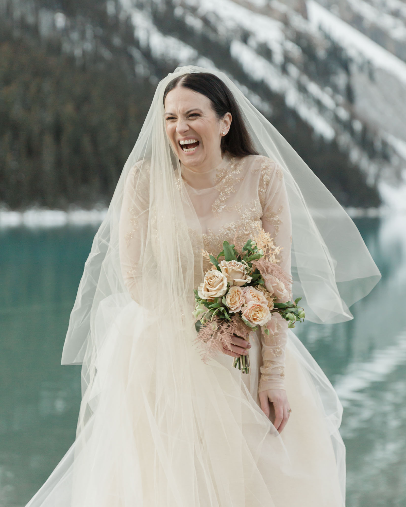 Bridal portraits in the mountains, she is laughing while holding her wedding bouquet