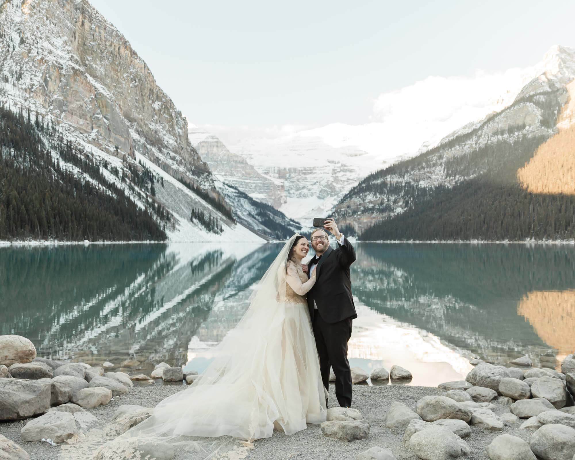 A Lake Louise elopement, the couple is taking a selfie in front of the winter wonderland in Banff