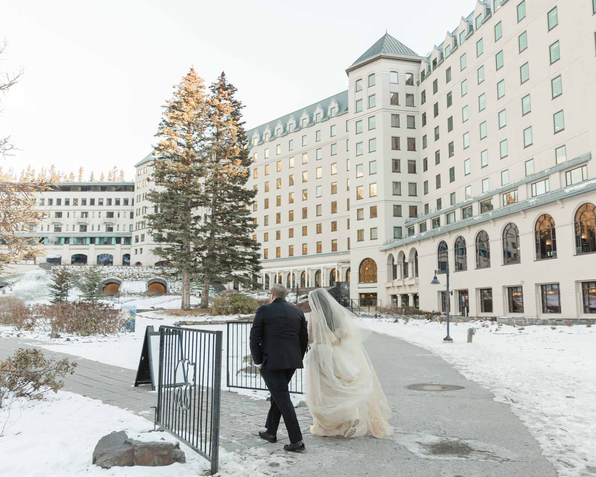 A couple walking towards the Fairmont Chateau Lake Louise after their ceremony at sunrise