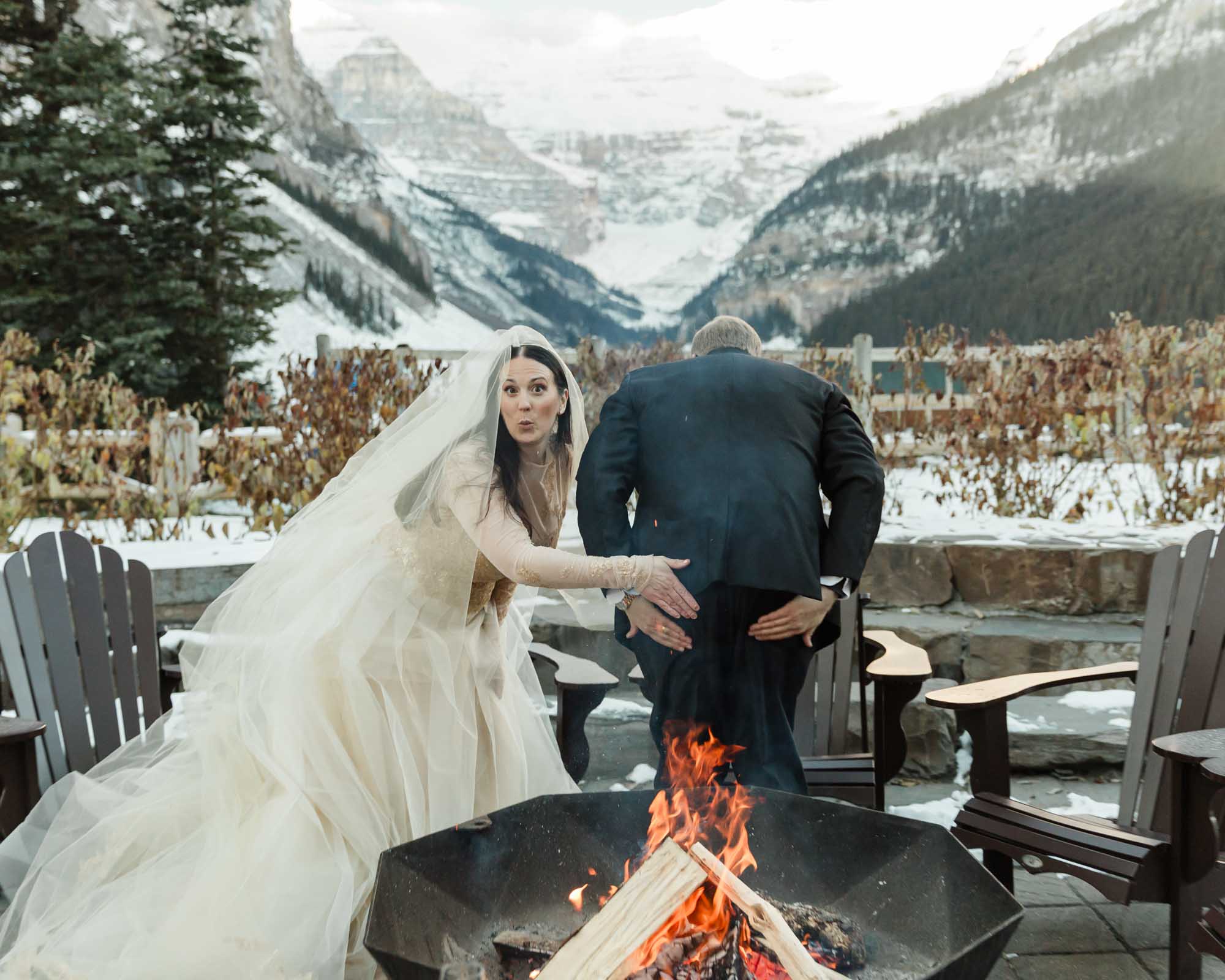 A couple is enjoying a bonfire in front of the Fairmont Chateau Lake Louise after their ceremony at sunrise
