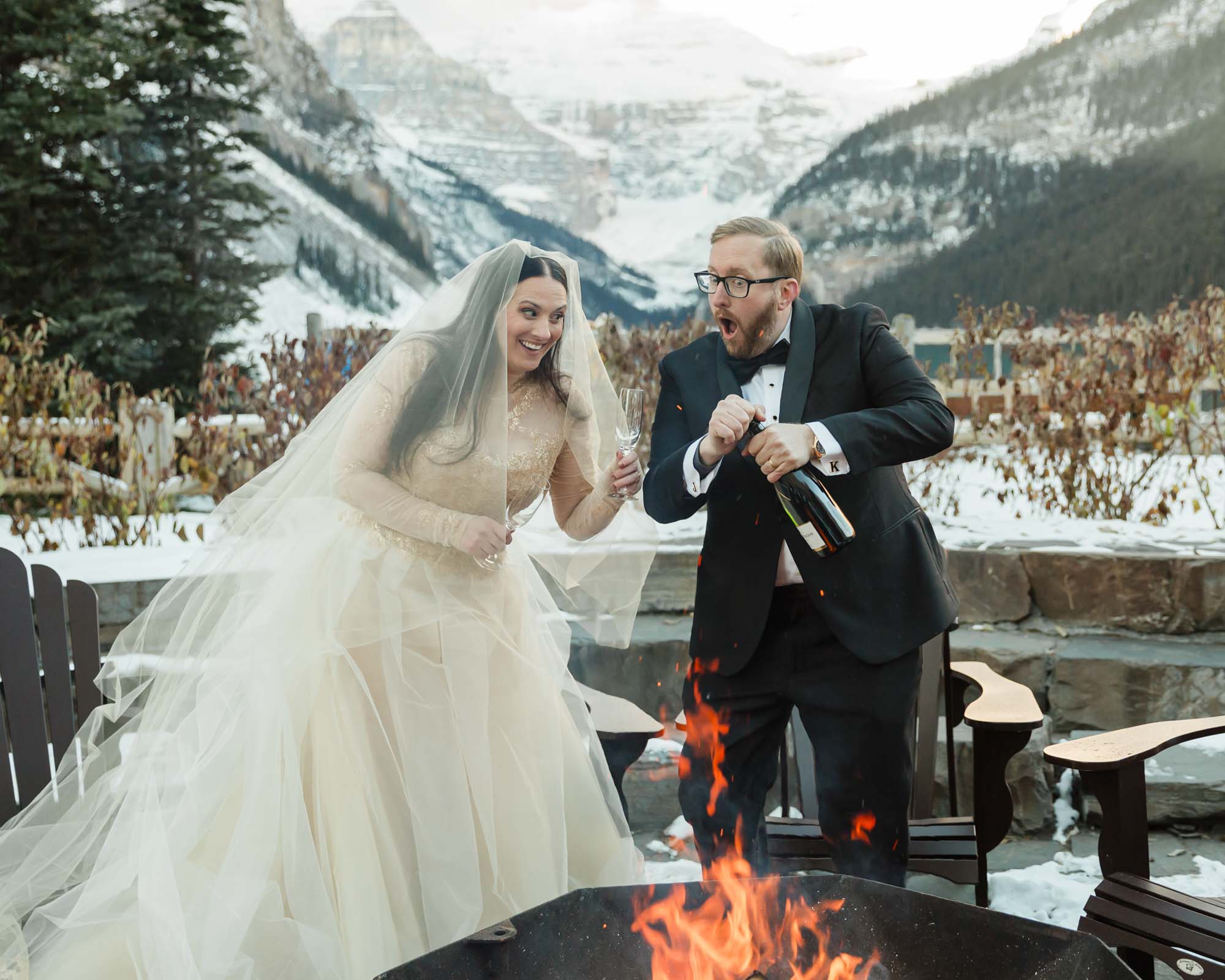 A couple is exchanging gifts and enjoying a bonfire in front of the Fairmont Chateau Lake Louise after their wedding ceremony at sunrise