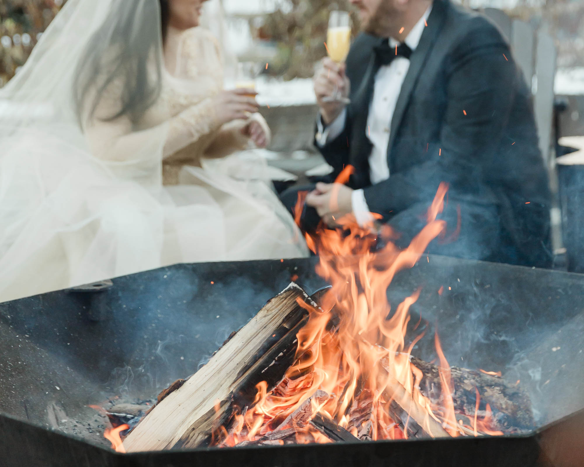 A couple is enjoying champagne and a bonfire in front of the Fairmont Chateau Lake Louise after their ceremony at sunrise