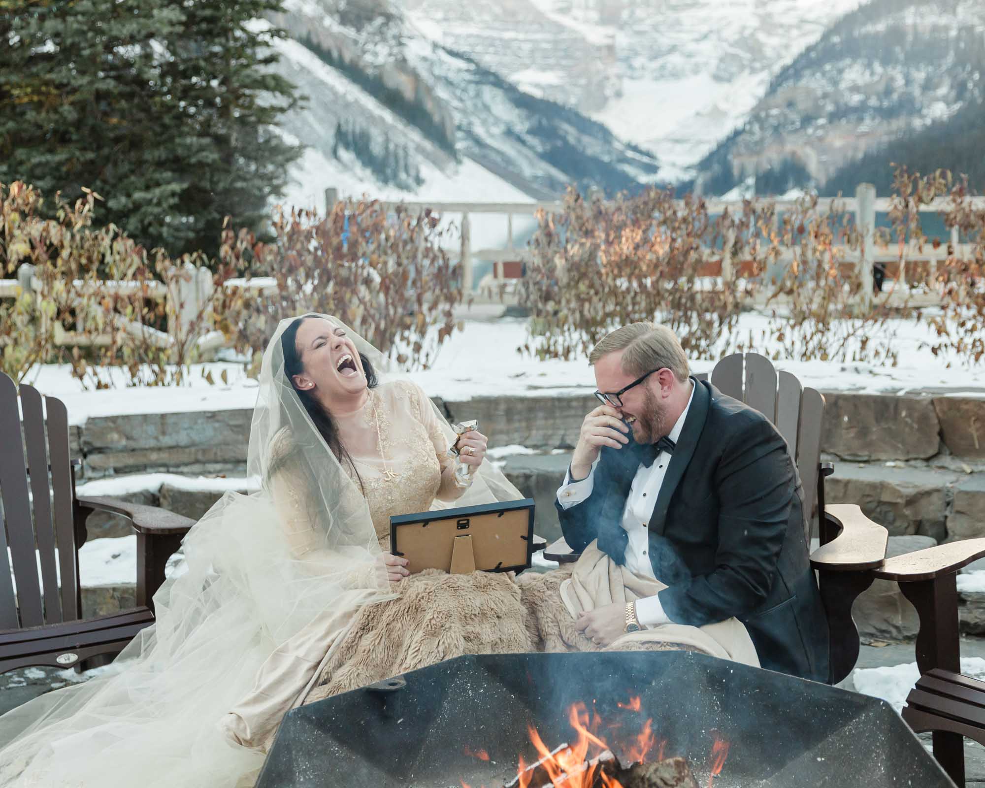 A couple is exchanging gifts and enjoying a bonfire in front of the Fairmont Chateau Lake Louise after their wedding ceremony at sunrise