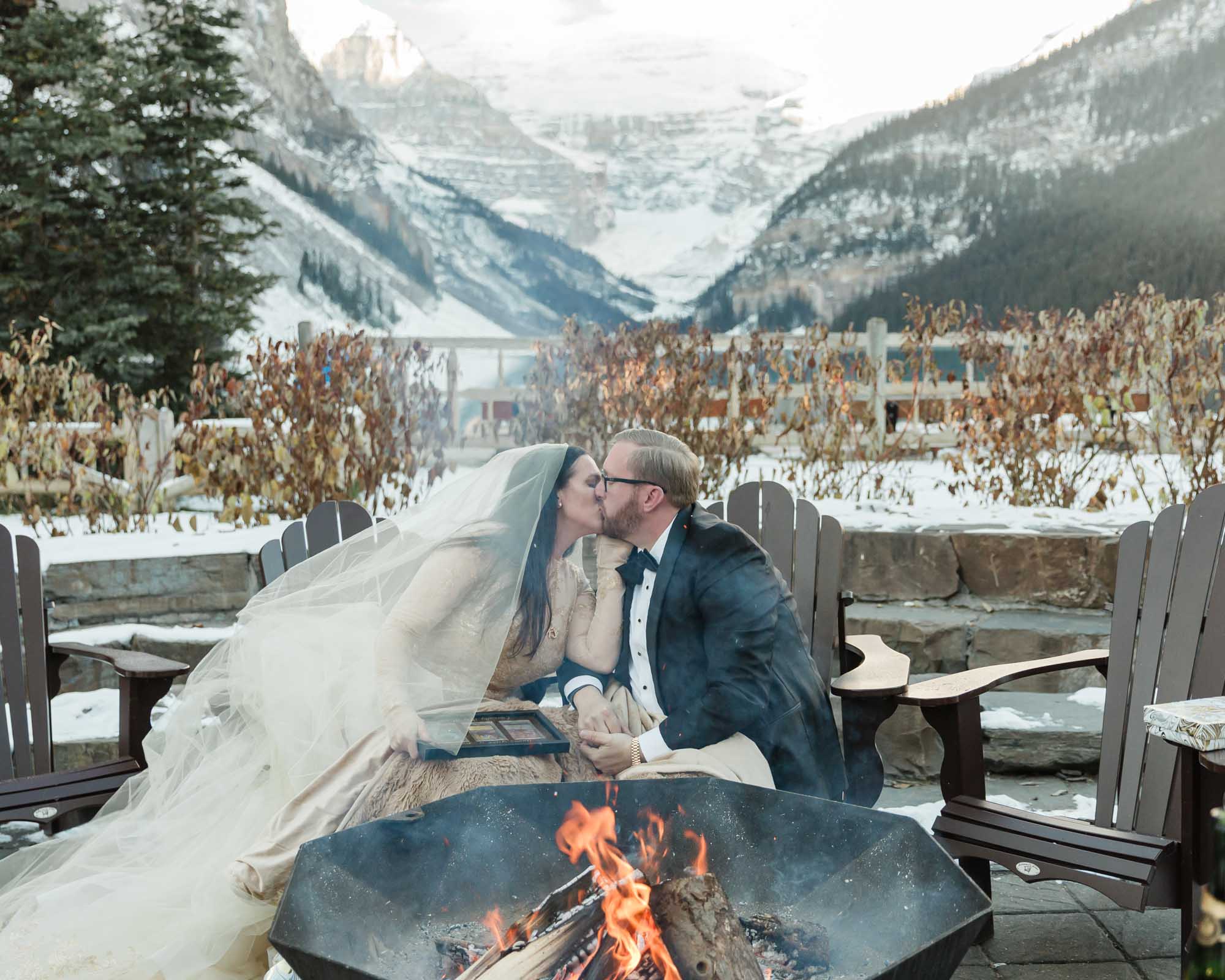 A couple is exchanging gifts and enjoying a bonfire in front of the Fairmont Chateau Lake Louise after their wedding ceremony at sunrise