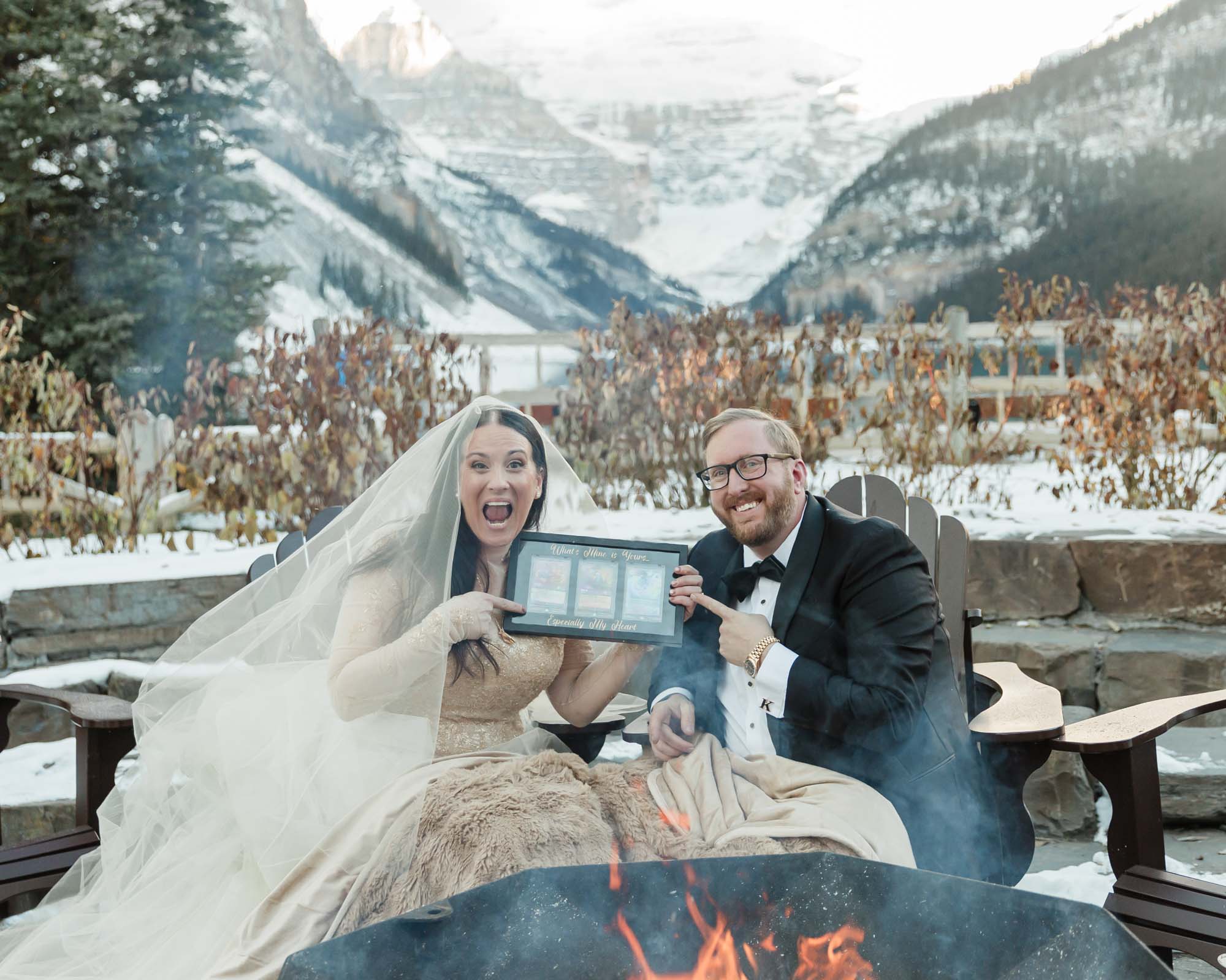 A couple is exchanging gifts and enjoying a bonfire in front of the Fairmont Chateau Lake Louise after their wedding ceremony at sunrise