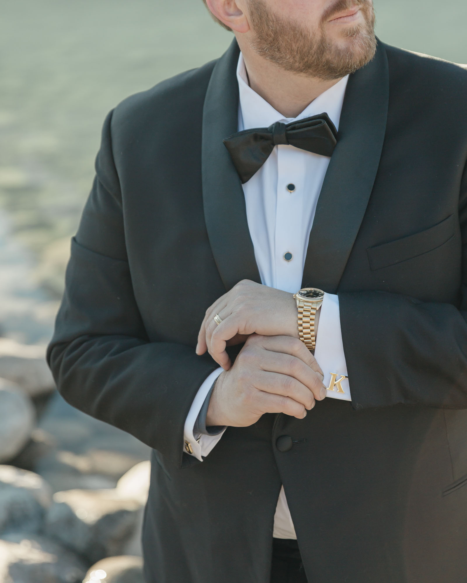 Groom portraits in front of the blue alpine waters for their mountain elopement with his watch accessory in focus