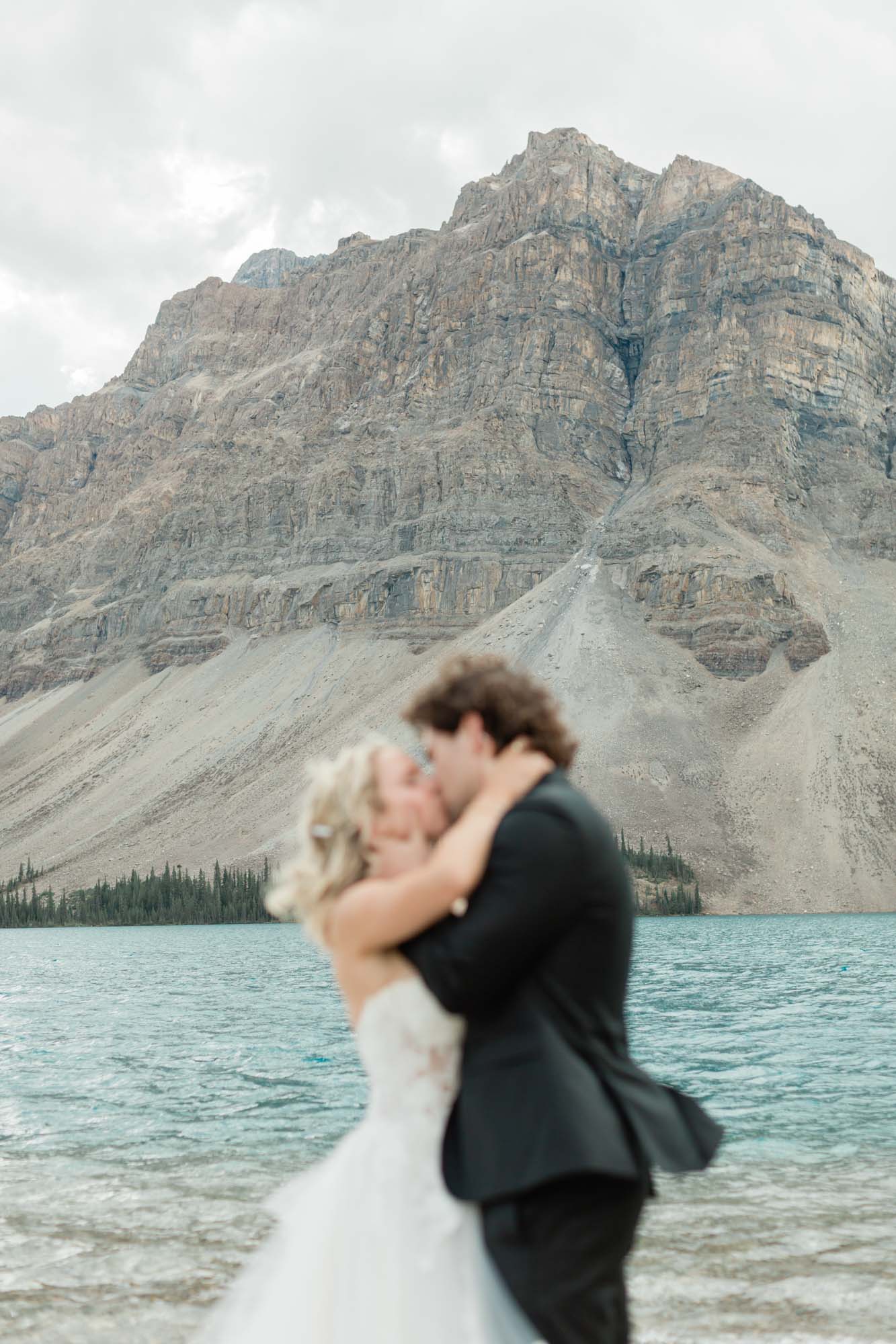 the couple hugging and kissing in front of the mountain after their wedding