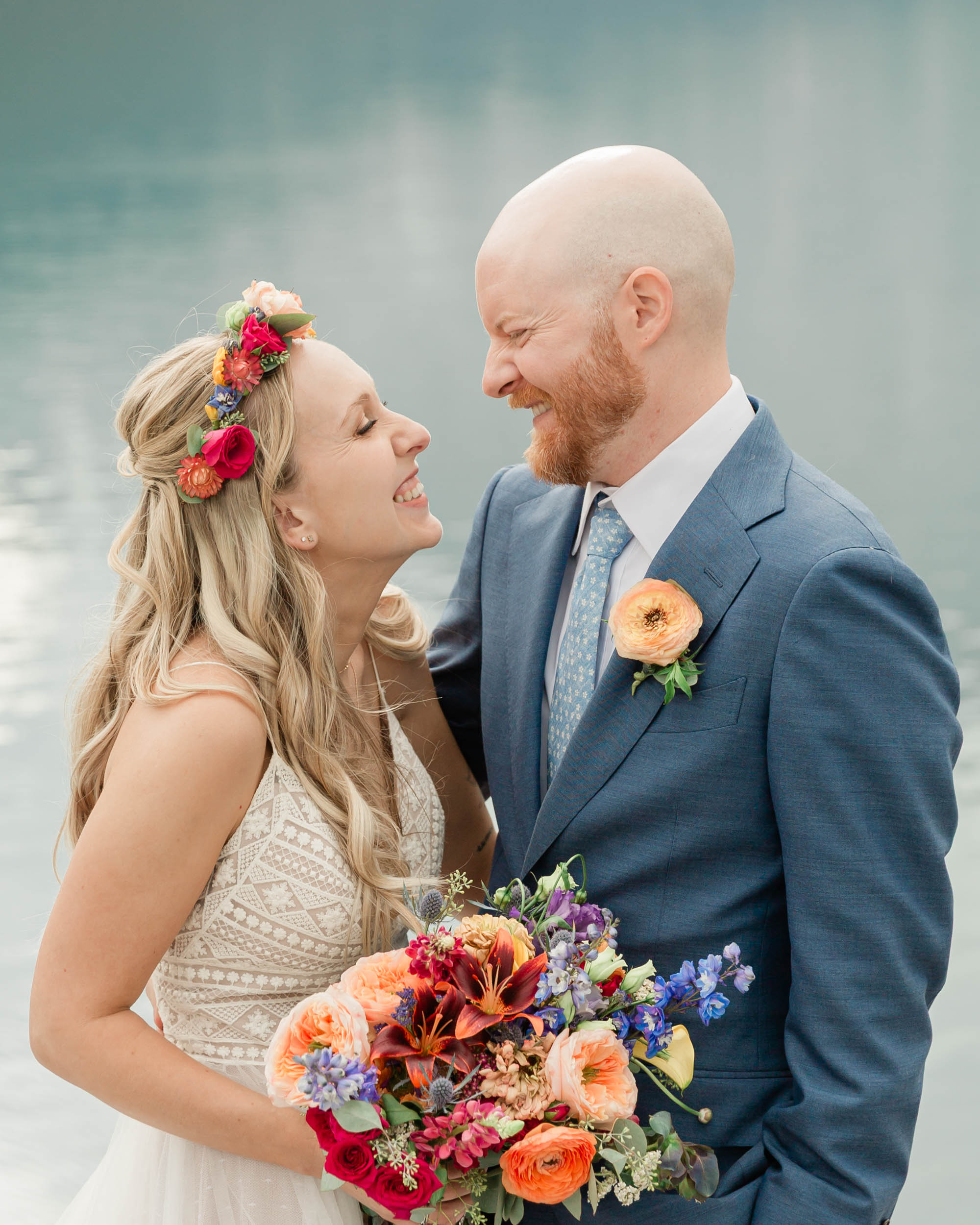 A bride and groom smiling and looking at each other, her in her wedding gown and him in his blue suit.