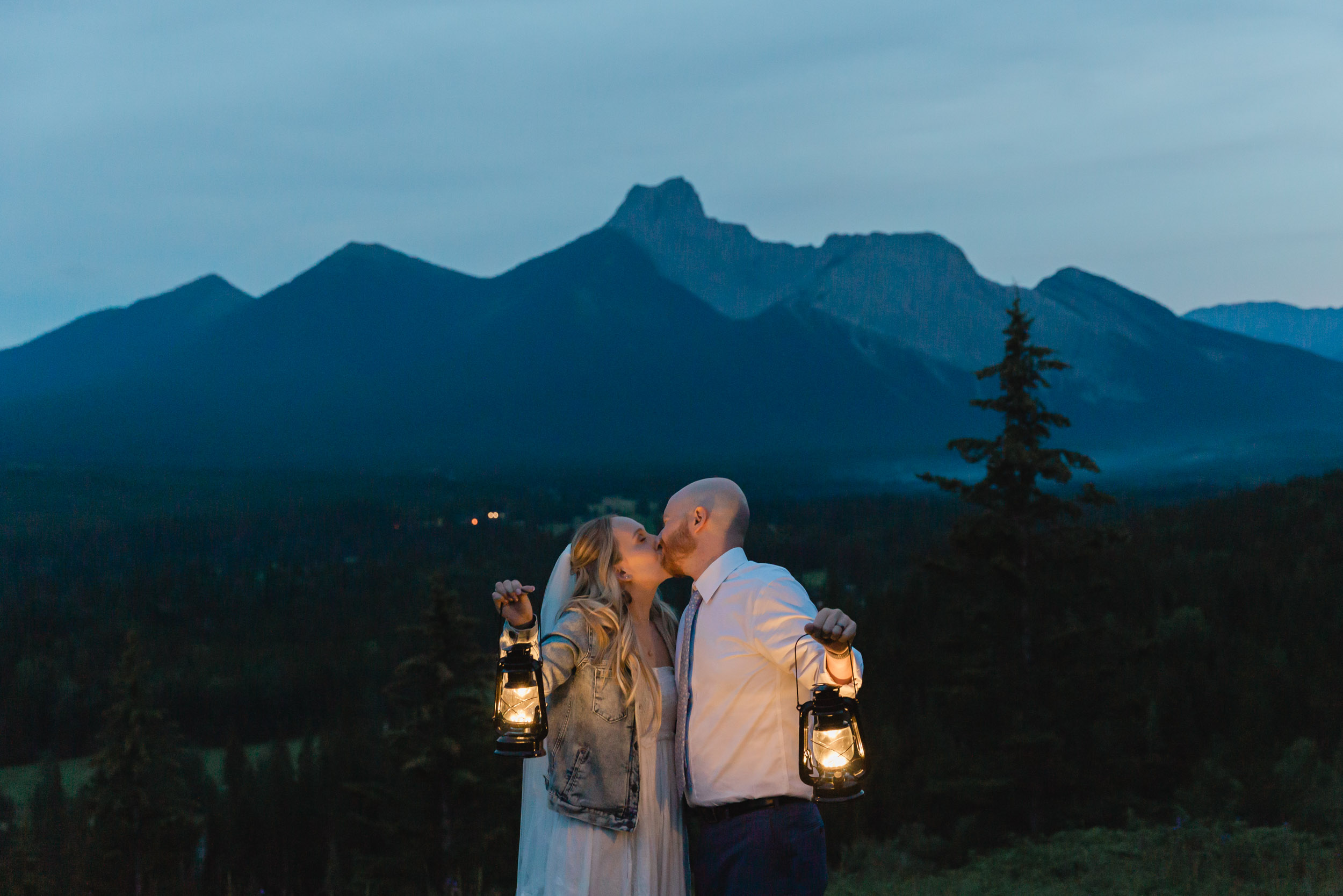 megan and scott holding lanterns at night time for their first dance with the banff mountain range behind them on their elopement day