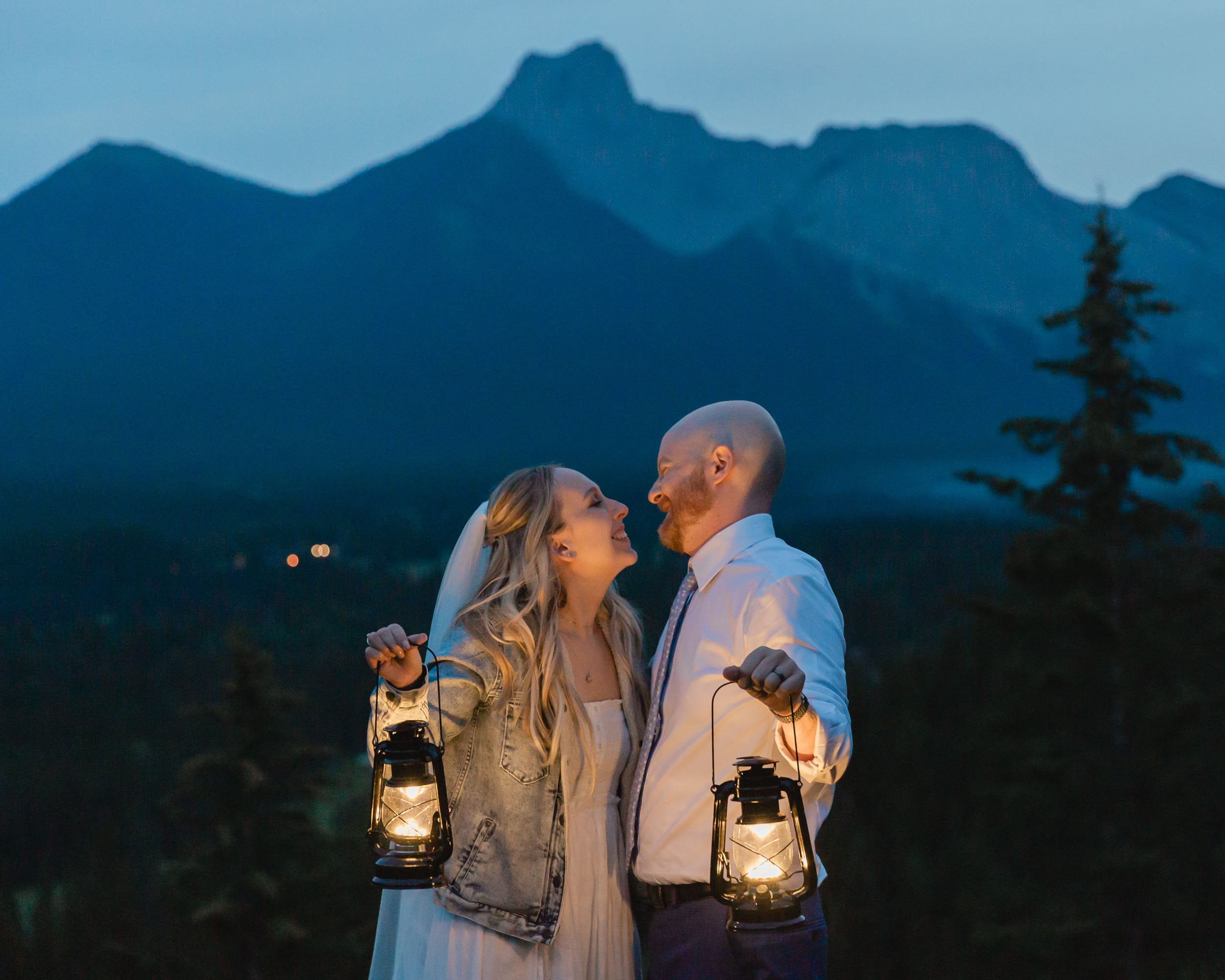 megan and scott holding lanterns at night time for their first dance with the banff mountain range behind them on their elopement day