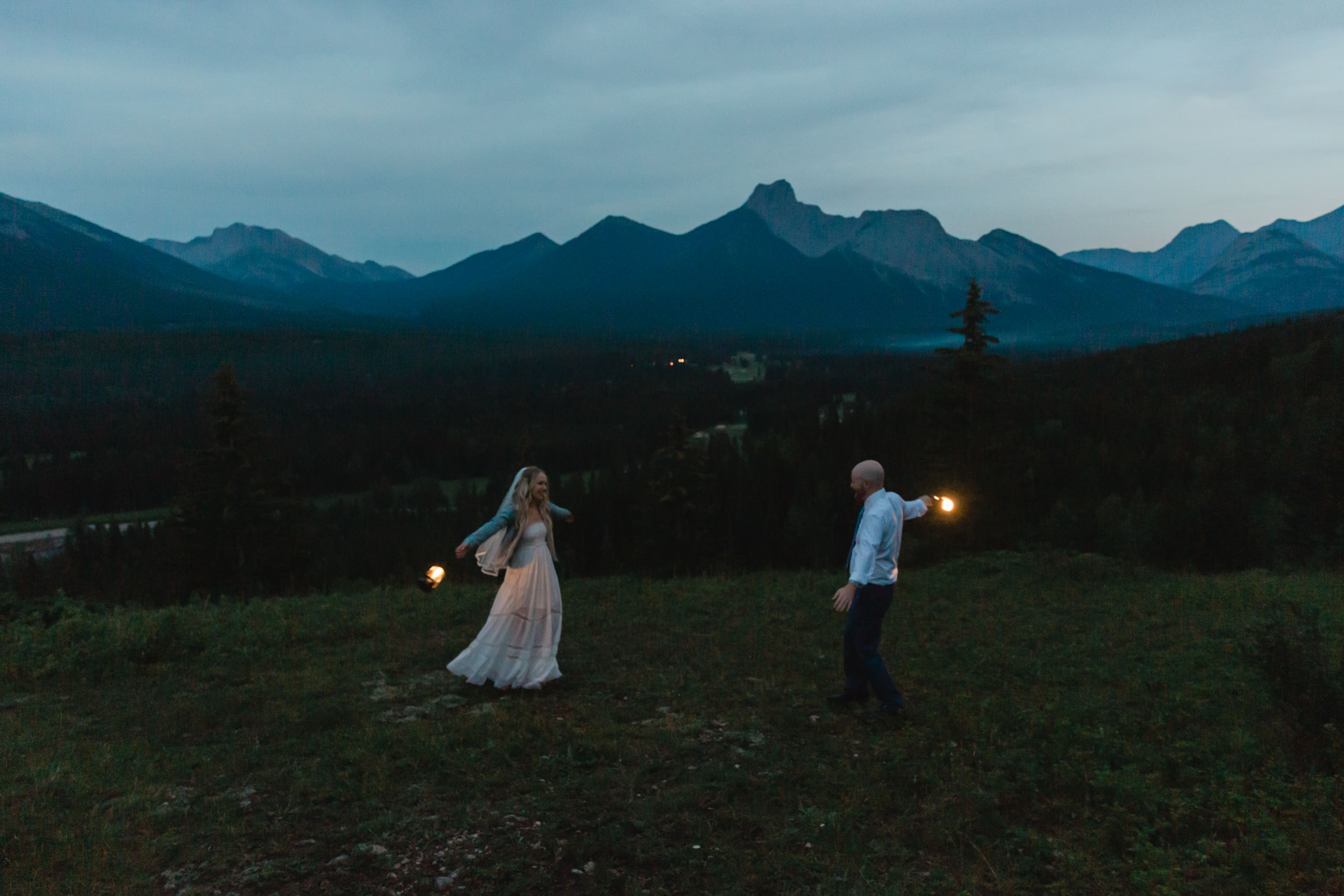 megan and scott holding lanterns at night time for their first dance with the banff mountain range behind them on their elopement day