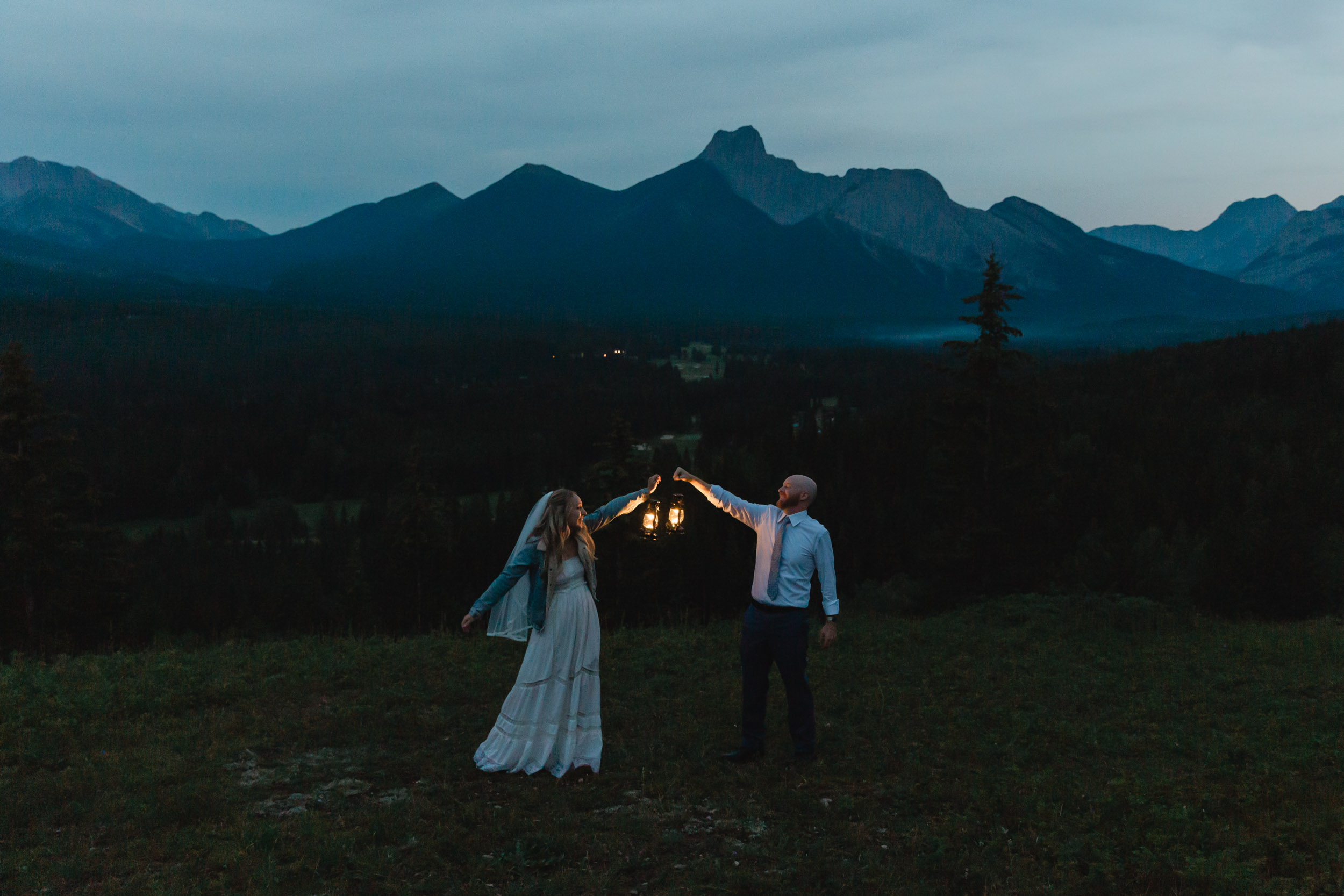 megan and scott holding lanterns at night time for their first dance with the banff mountain range behind them on their elopement day