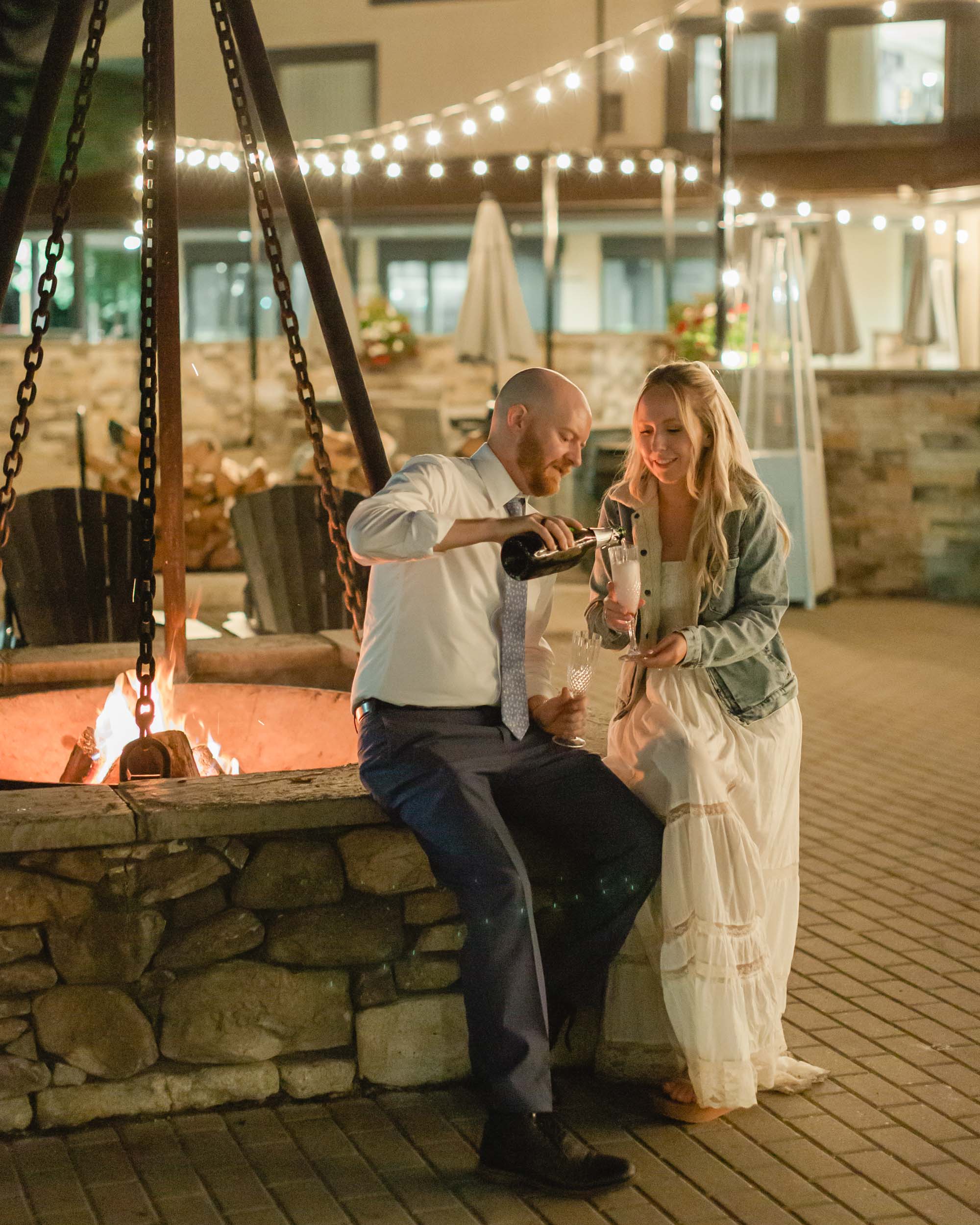 couple celebrating after their mountain elopement with champagne and smores in front of a bonfire
