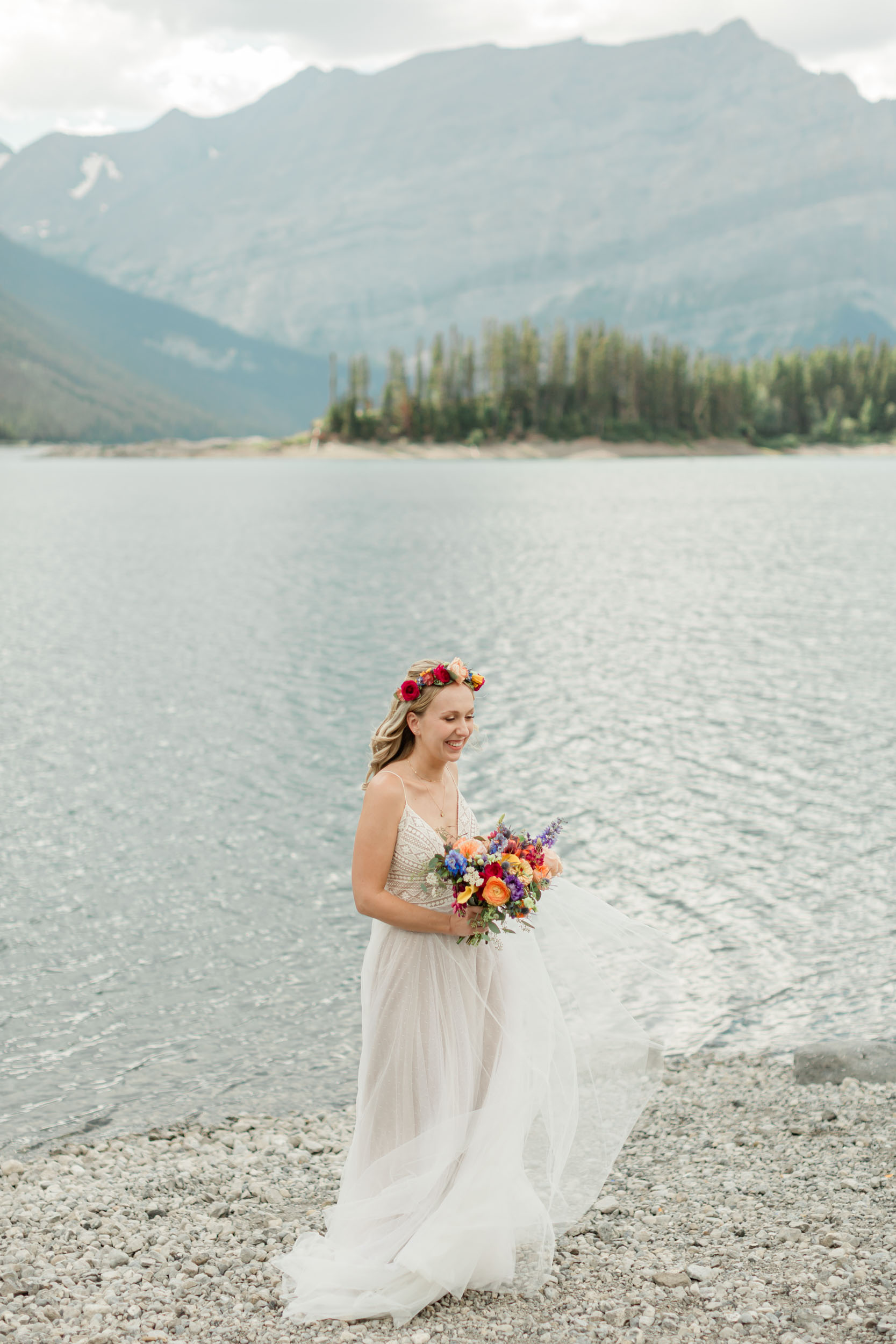 the bride is laughing and spinning smiling during her portrait in front of the alpine lake and mountain views