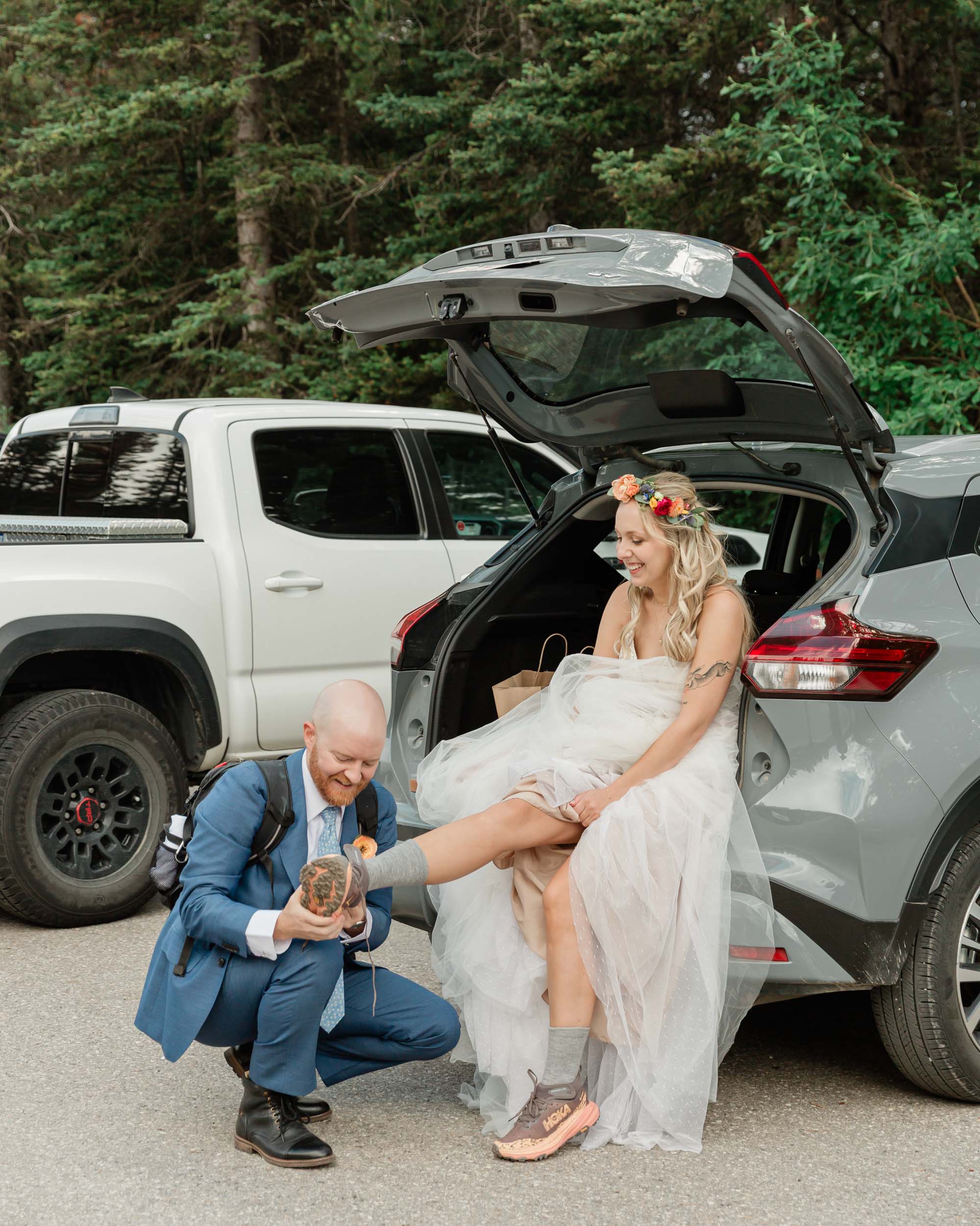 the groom helping the bride with her hiking shoes before adventuring to their ceremony mountain wedding