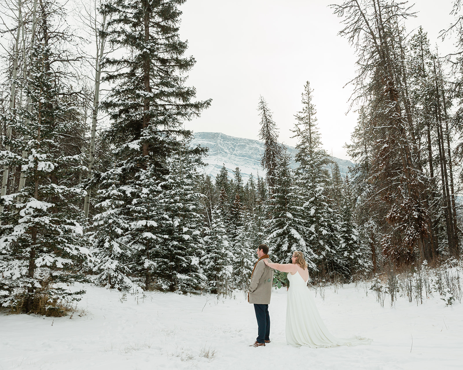 Couple sharing a snowy first look surrounded by pine trees during their Banff winter elopement in Banff National Park.