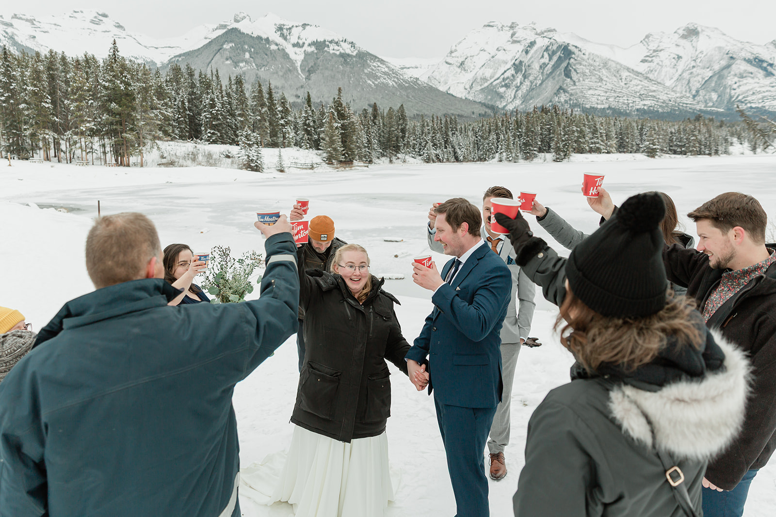 Newlyweds and guests raising hot chocolate for a celebratory toast during a snowy Banff winter elopement in the Canadian Rockies.