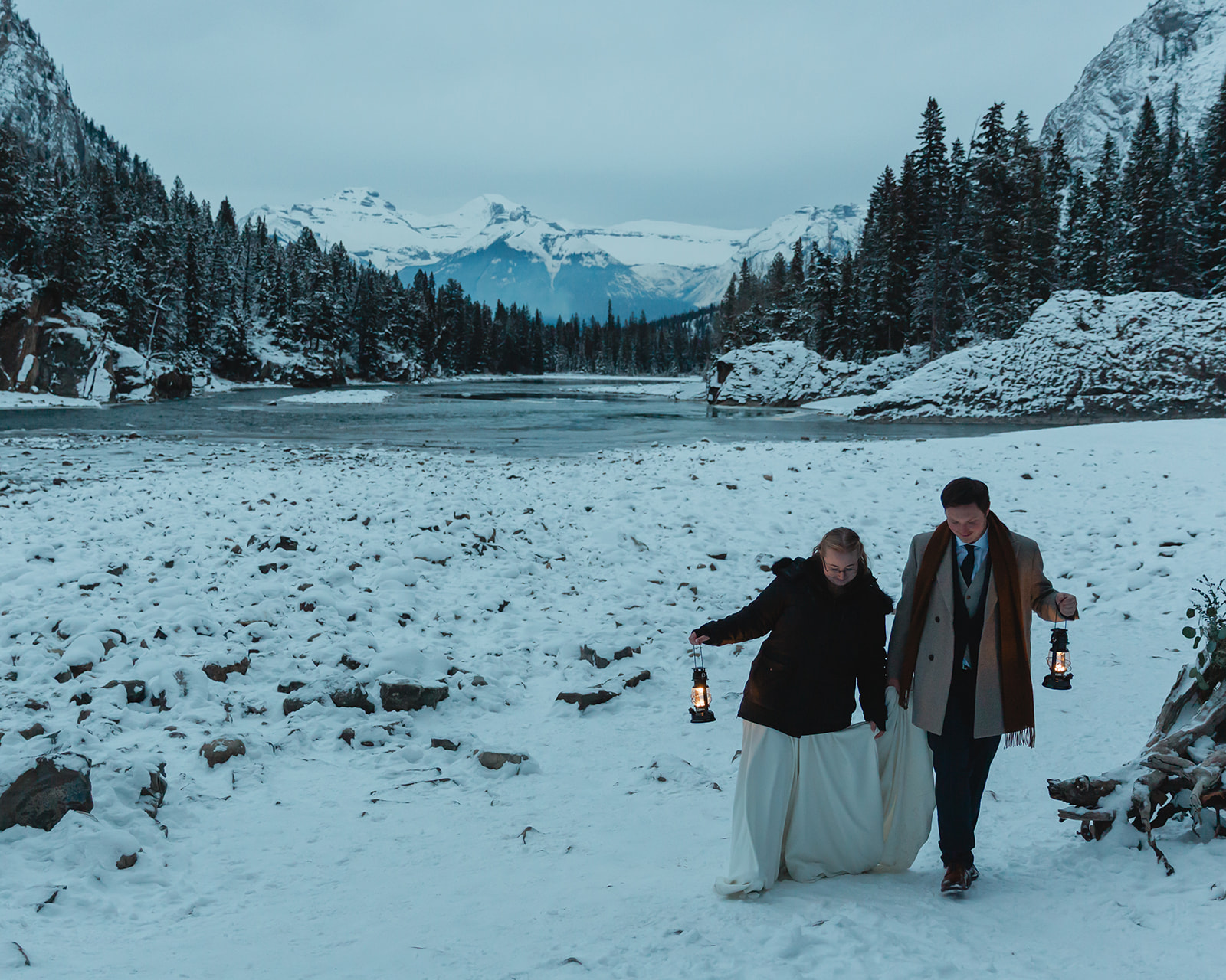 Couple walking with lanterns through the snow during their Banff winter elopement at Bow Falls in Banff National Park.