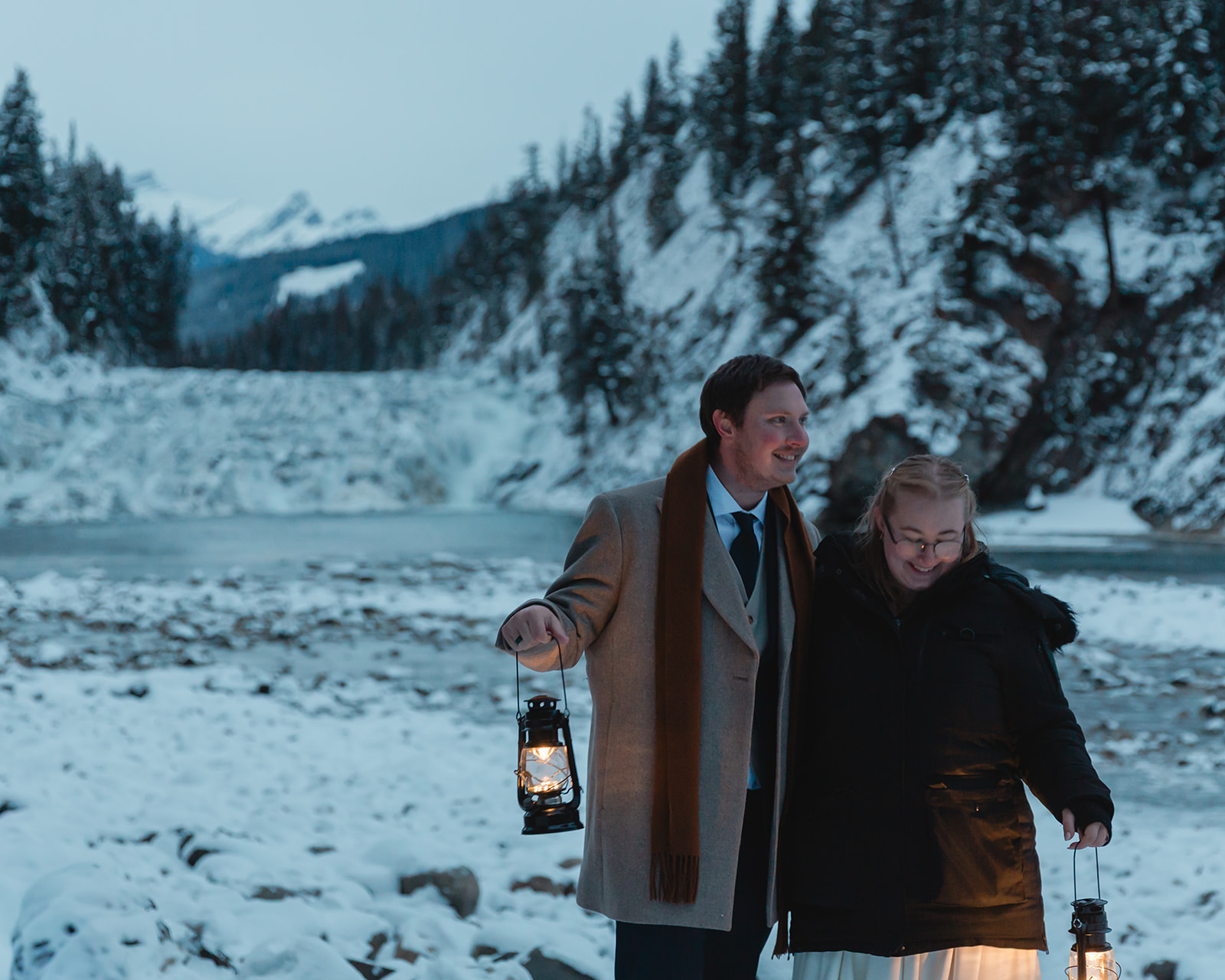Gabriella and Bronson hold glowing lanterns at Bow Falls during blue hour on their snowy Banff winter elopement day.