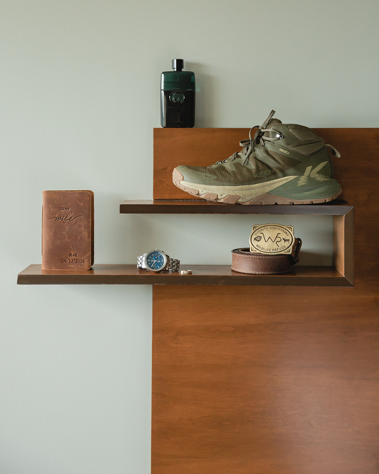 Groom’s hiking boots, personalized vow book, watch, belt, and cologne arranged before a Lake Minnewanka elopement in Banff.