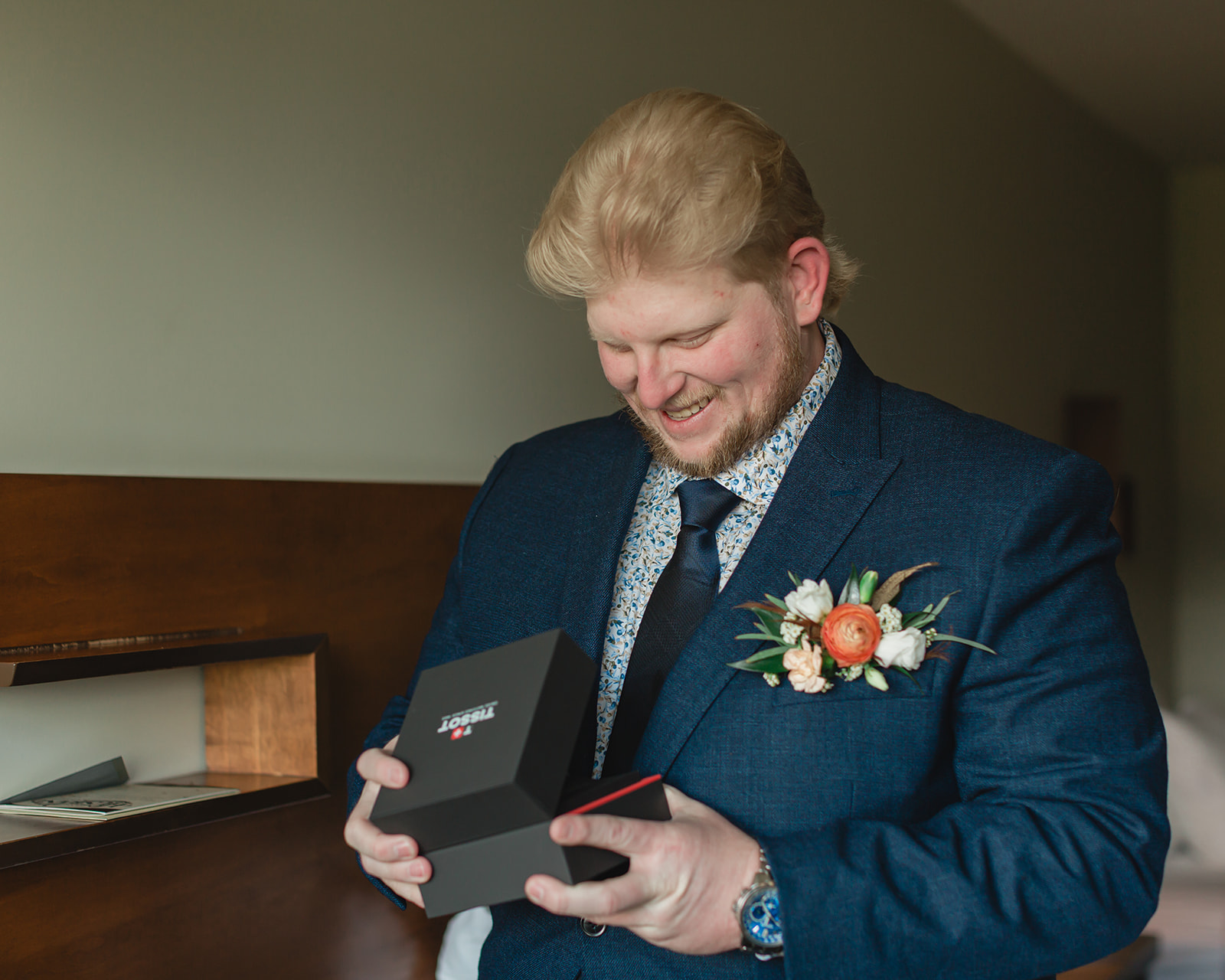 Groom smiling as he opens a gift while getting ready for his Lake Minnewanka elopement in Banff.