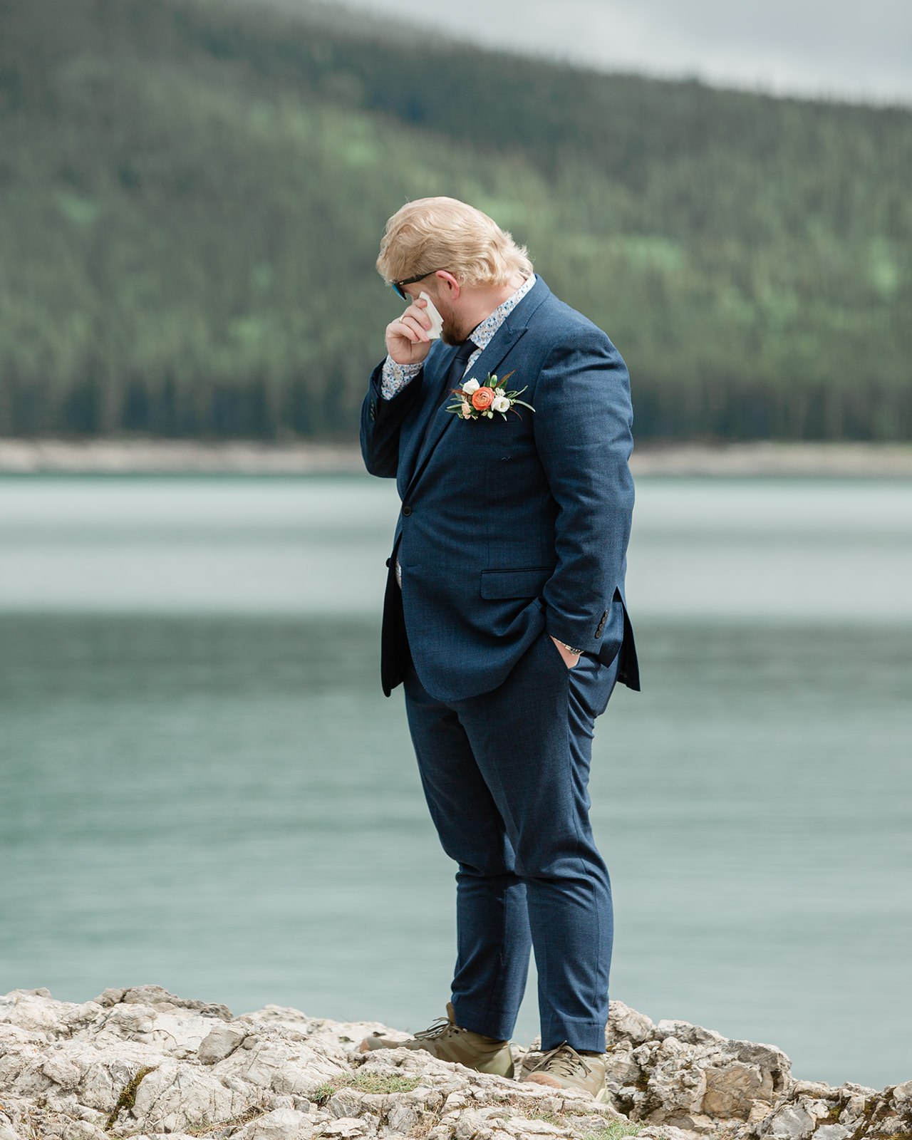 Groom wiping away tears as he waits for his bride on the Lake Minnewanka shoreline during their Banff elopement.