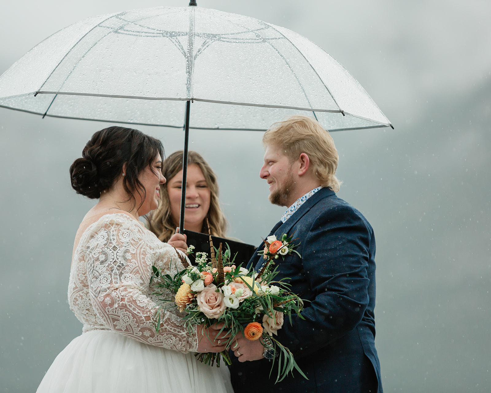 Couple smiling beneath a clear umbrella during their rainy Lake Minnewanka elopement ceremony in Banff National Park.