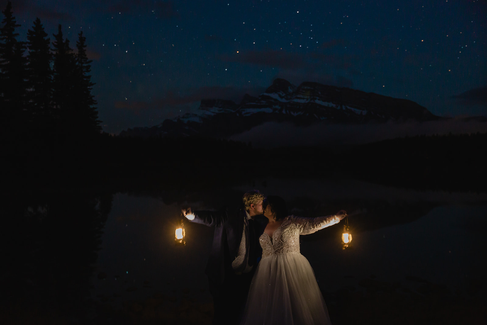 Rachel and Russell kiss while holding glowing lanterns beneath a star-filled sky during their Banff elopement, with the Canadian Rockies silhouetted behind them.